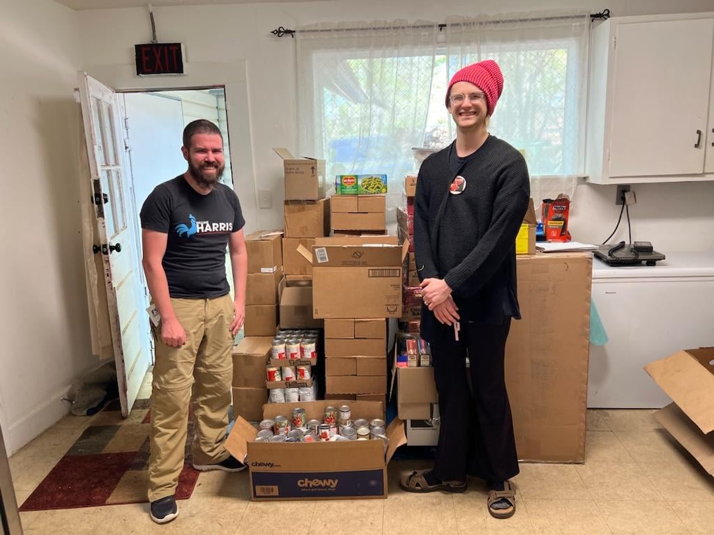 Zachery Fuller and William Harris standing and smailing in front of a large stack of canned food donations.